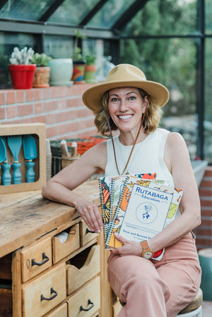 Kaitlin Mitchell, founder and CEO of Rutabaga Education and Rutabaga tools. She is posing in her garden with her education books and garden tools.